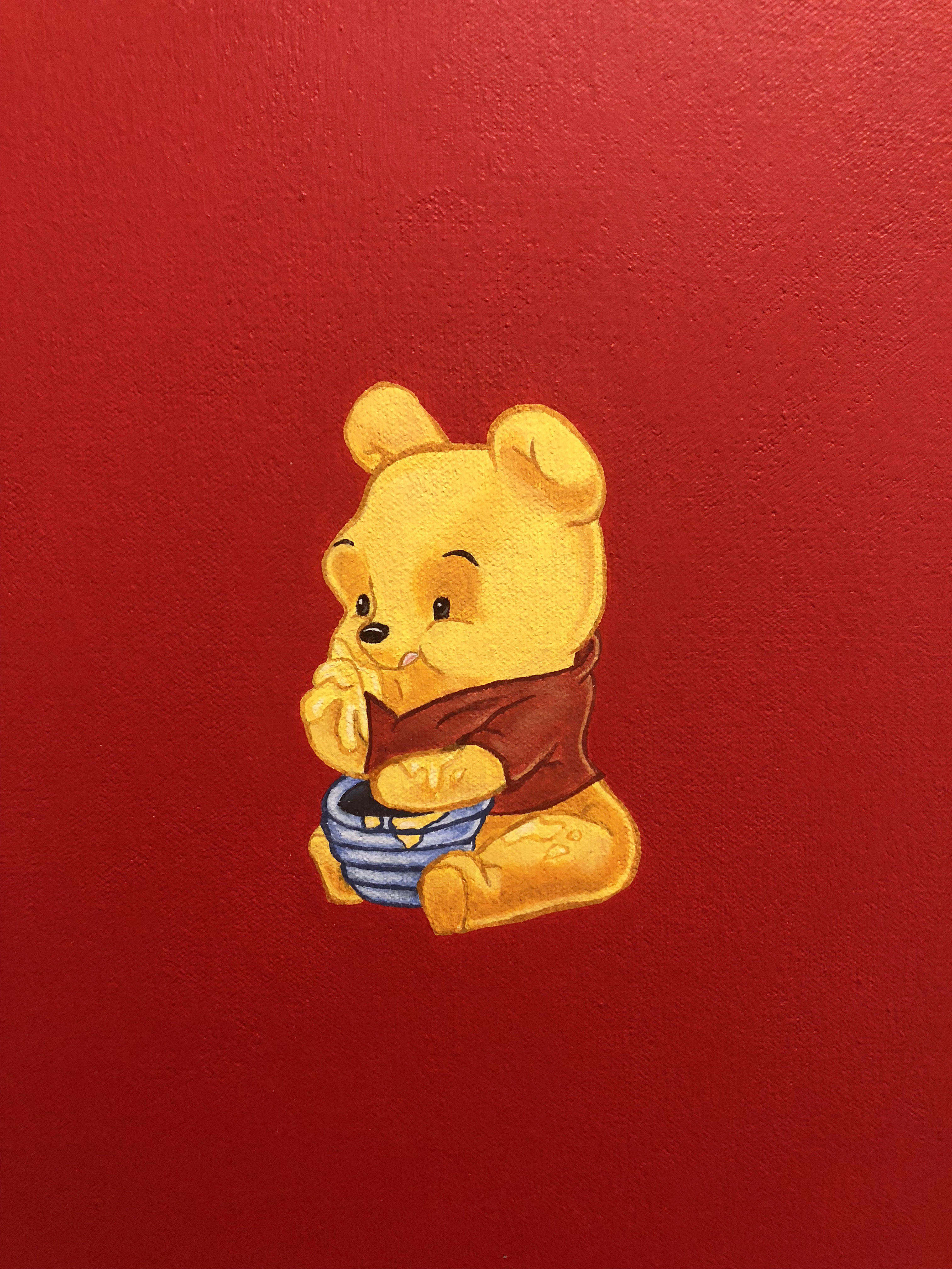 Detail of a painting of winnie the pooh eating honey out of a pot on a red background hung on a white wall